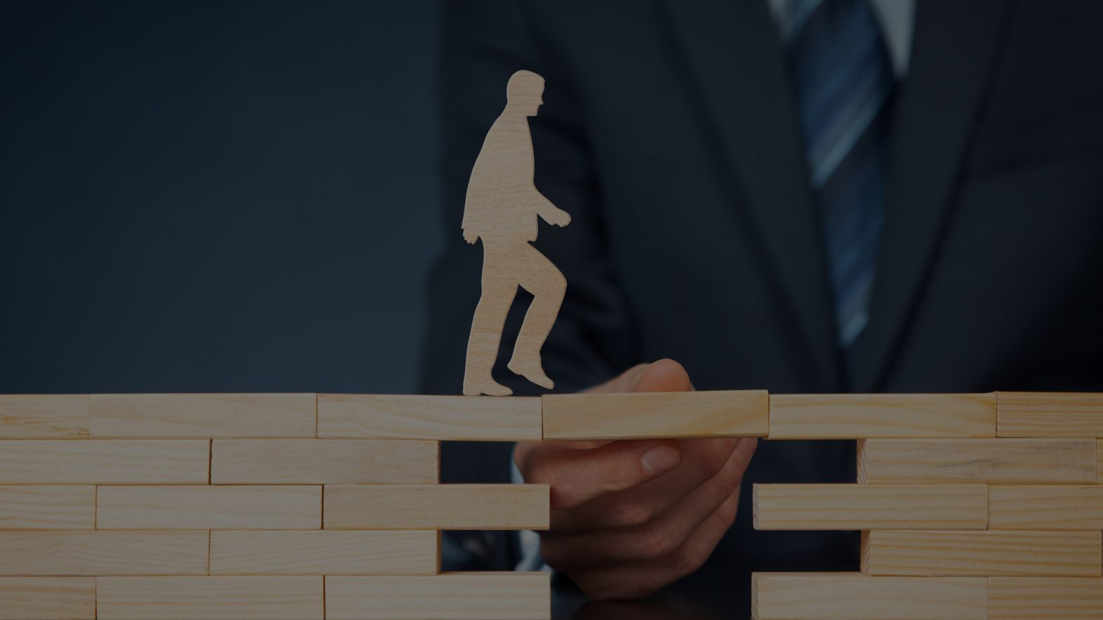 Wooden figure of man walking over jenga blocks being held up