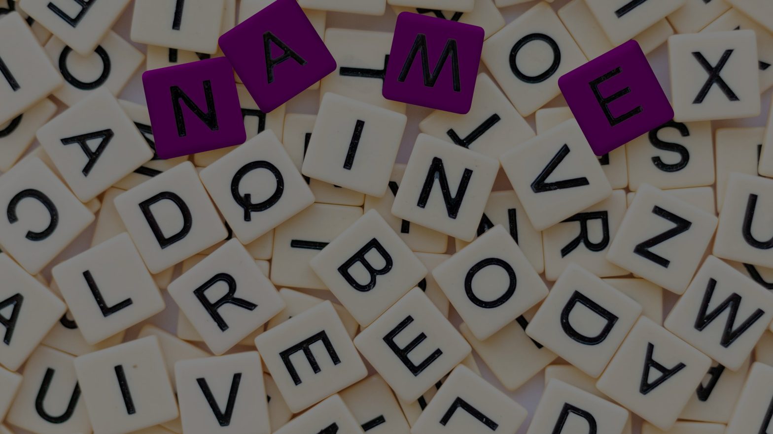 Scattered scrabble pieces with purple ones spelling "name"