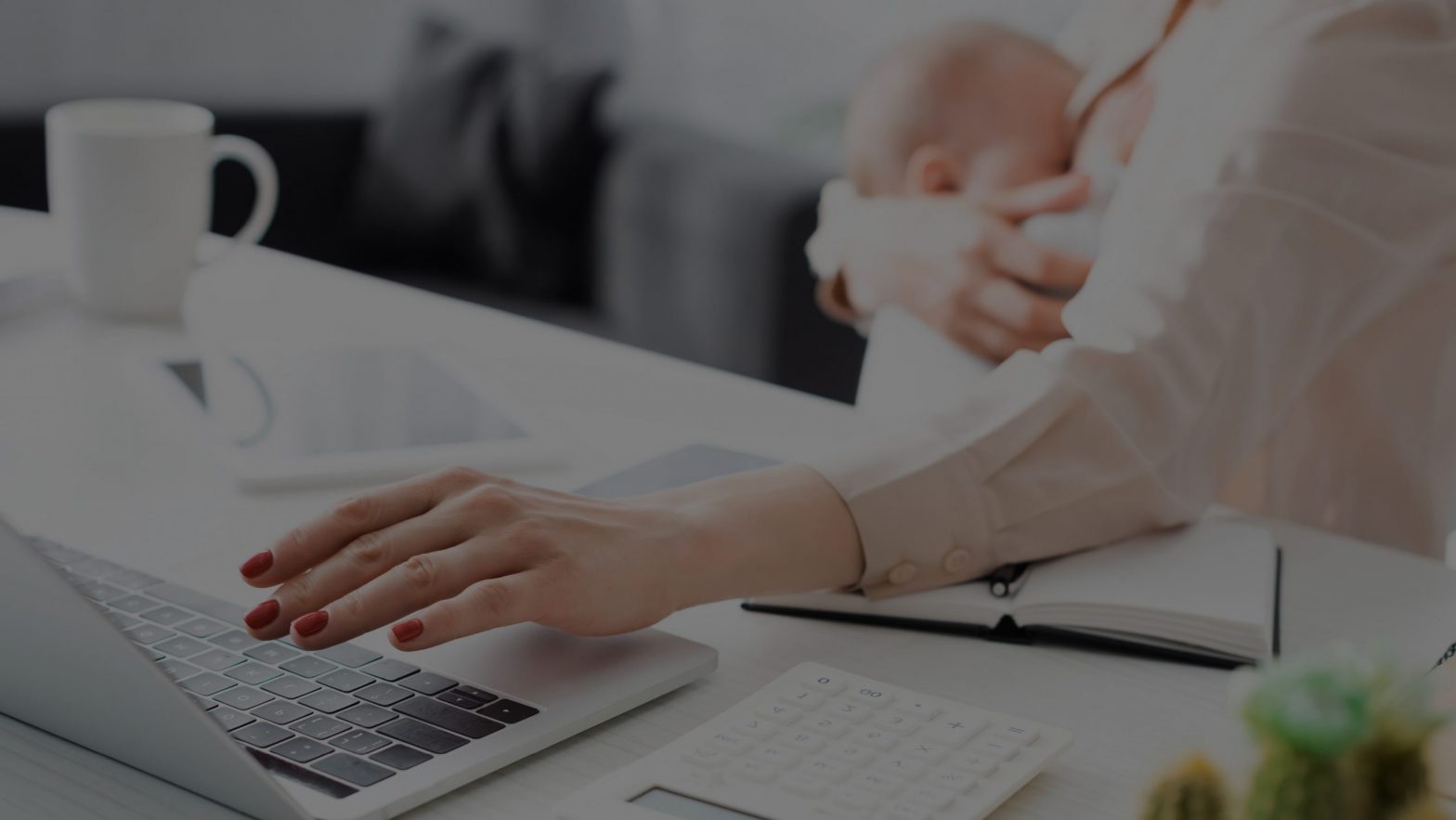 Woman holding baby while working at a laptop